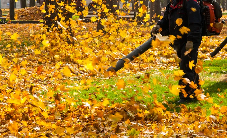 a stock photo of a man in dark clothes using a leaf blower