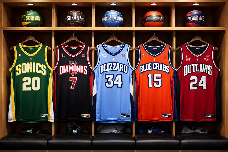 Fictitious jerseys of the Seattle Sonics, Las Vegas Diamonds, Buffalo Blizzard, Baltimore Blue Crabs, and Kansas City Outlaws hang from locker room lockers with matching team basketballs sitting above them.