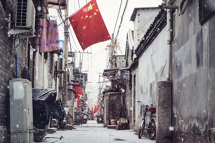 A Chinese flag overhanding and urban street with snow falling.