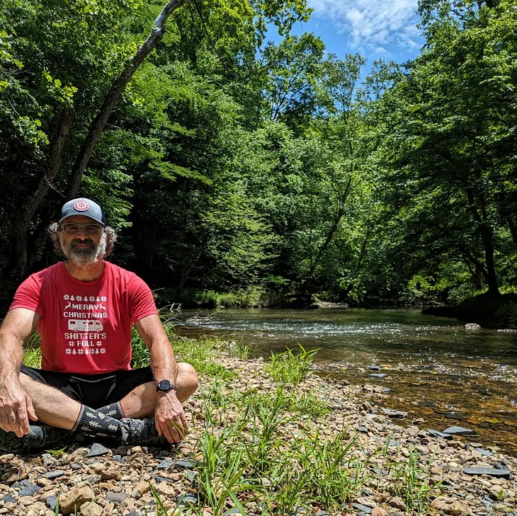 The author sitting crosslegged on a bed of rocks by a shallow creek.