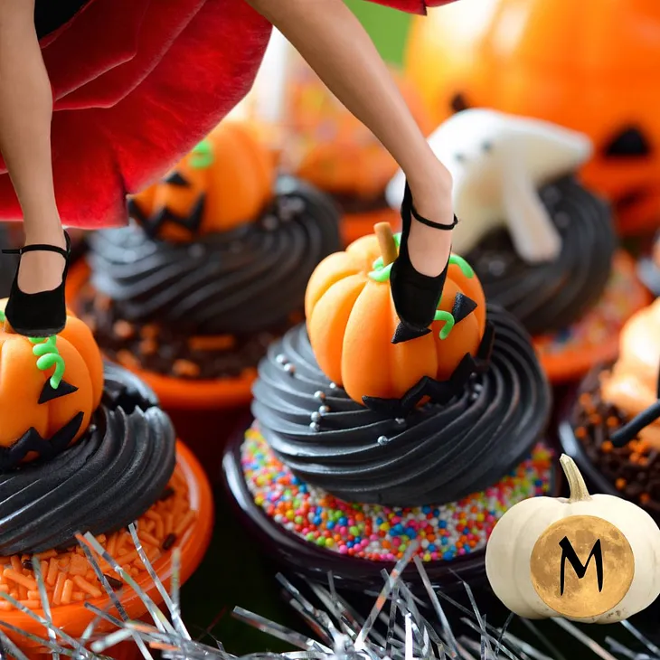 a flamenco dancers feet land on top of two precious uber-decorated Halloween cupcakes repleat with icing pumpkins sitting on nests of black icing with groves in them. other cupcakes sport ghosts and more pumpkins.