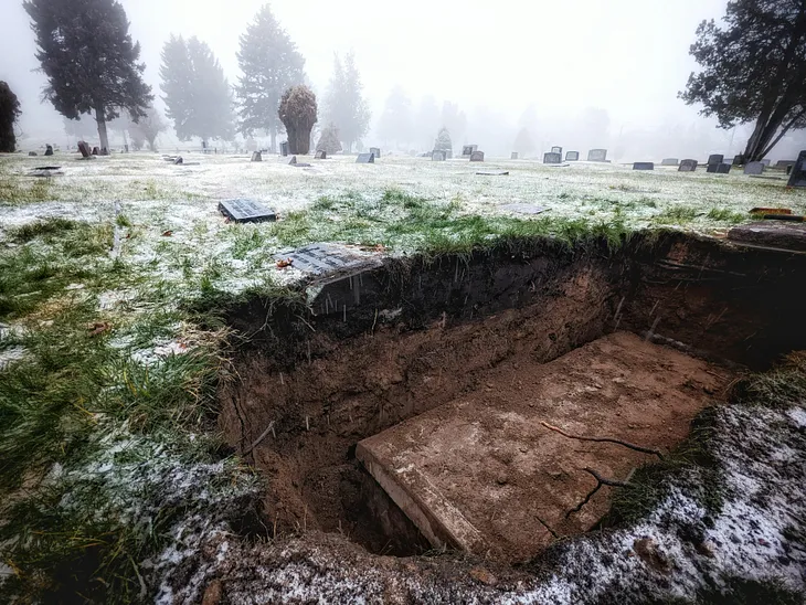 A snow covered field with an old casket in an open grave