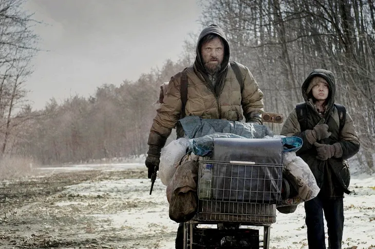 The image depicts two individuals with their faces obscured, in a desolate, snowy landscape. One person is pushing a cart filled with various items, while the other walks alongside. They are both dressed in heavy clothing, suggesting cold weather.  The image evokes a sense of desolation and hardship. It could be interpreted as a scene from a post-apocalyptic or dystopian story or a reflection of the current state of the world