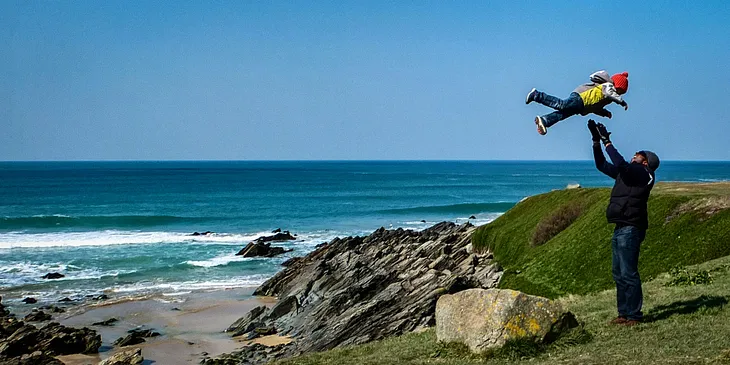 A father plays with his daughter by the sea, throwing her into the air