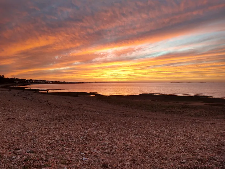 A photograph of the beach with the sea meeting the horizon at sunset.