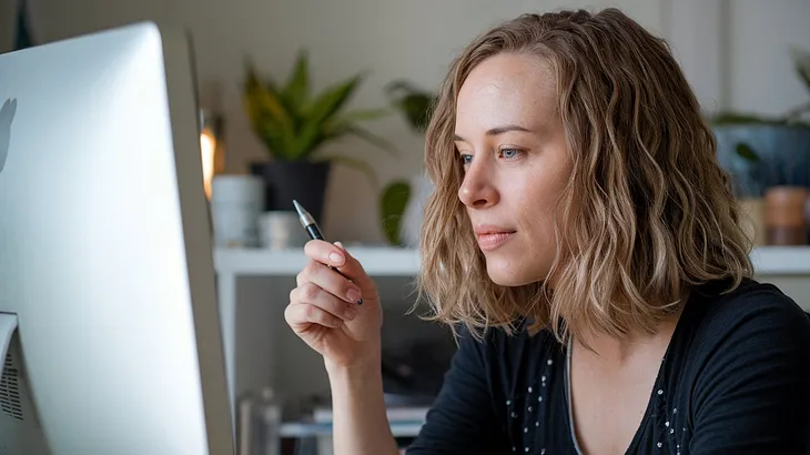 Woman in front of computer, contemplating the screen.