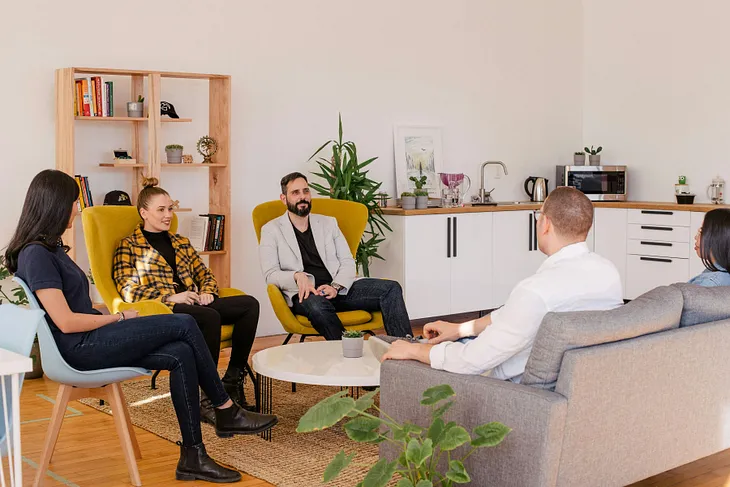 A group of people sit around an office area, talking.