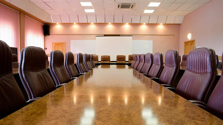 A large boardroom table with leather chairs lined up on each side of the table.