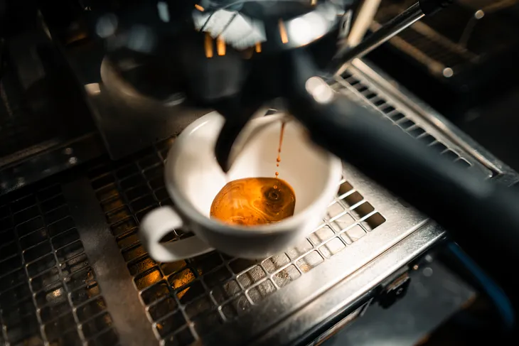 Close-up of espresso being extracted into a white cup from an espresso machine.