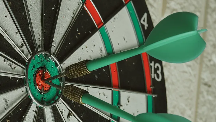 A dart board with two darks hitting the bullseye (center of the dart board).