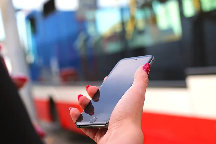 Woman’s hand holding a smart phone near a bus