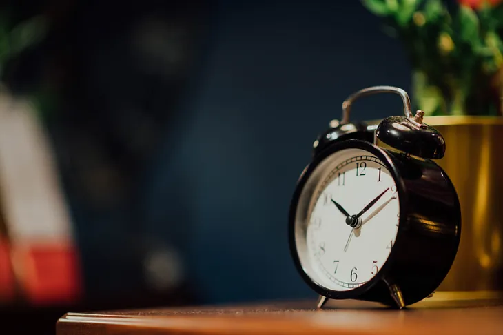 A black alarm clock rests on a dusty bedside table