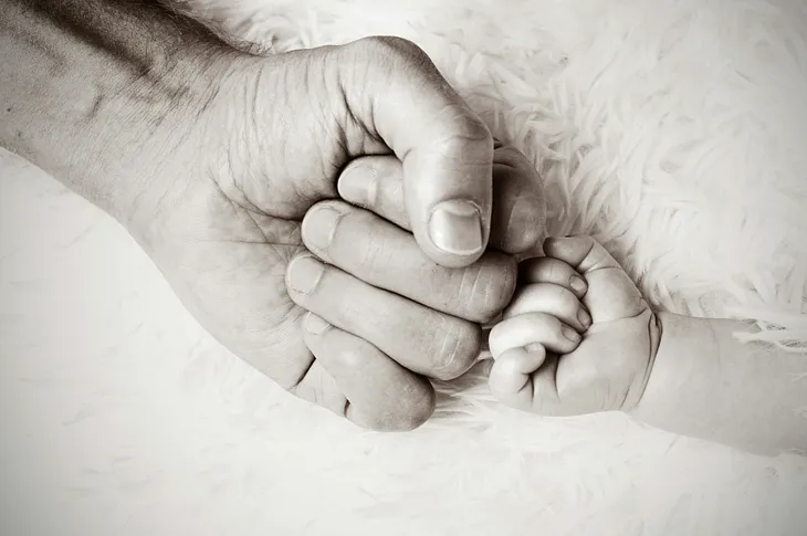 Photo of a parent’s or grandparent’s fingers touching the fingers of a baby.