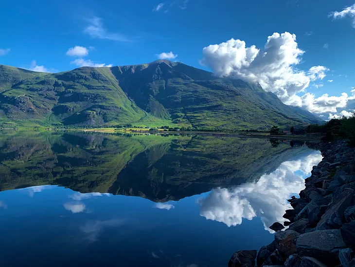 Mountains reflect crisply in the still sea loch below on a blue bird summer day