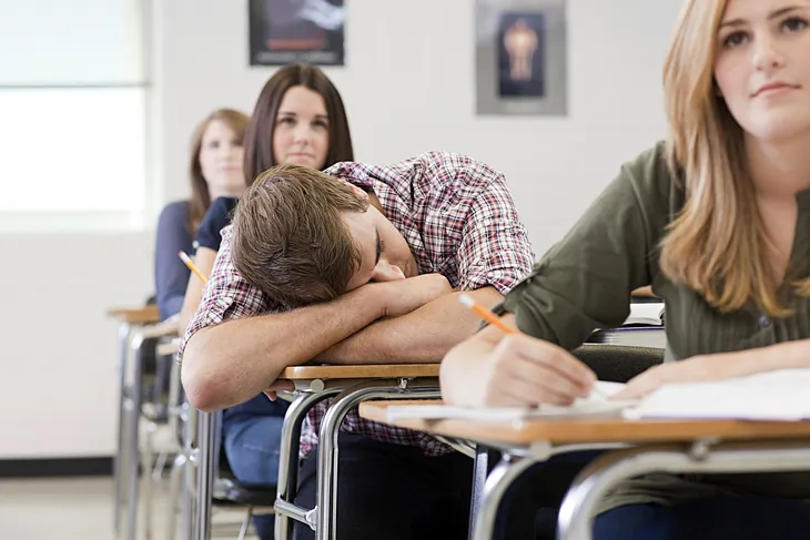 High school student dozing off during class while others pay attention