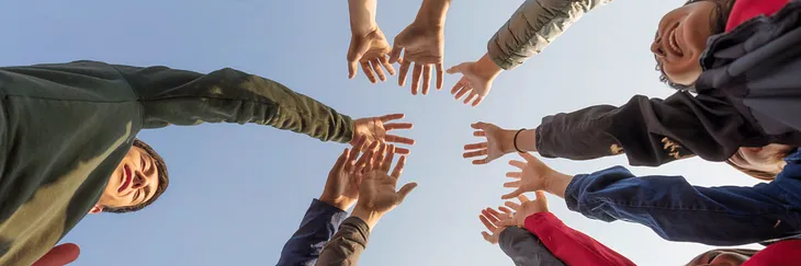 Photo from below showing ten hands outstretched to the clear blue sky and two boys in the frame for the article Practical Ways to Build Community Overcoming Isolation and Creating Strong Communities Through Connection by Gem Blackthorn