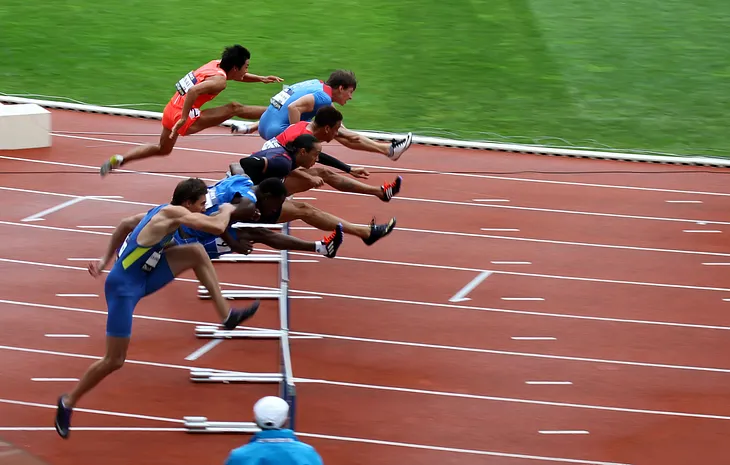 Athletes jumping over a hurdle in a race