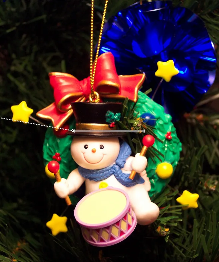 Image of a toy snowman decoration, beating a drum on Christmas tree.