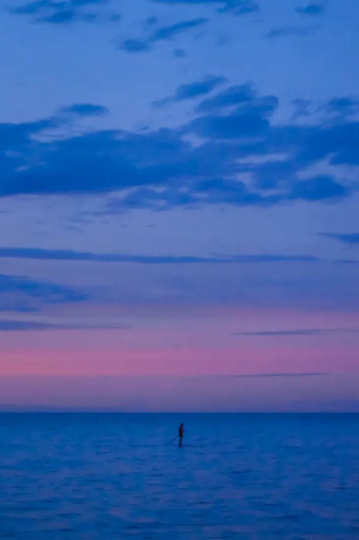 Float—a paddle boarder gliding across the lake at blue-pink sunset sky | nature photography | © pockett dessert