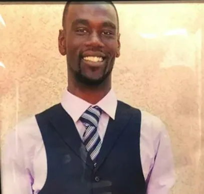 photograph of smiling Black man in a light pink shirt, striped tie, and charcoal suit vest