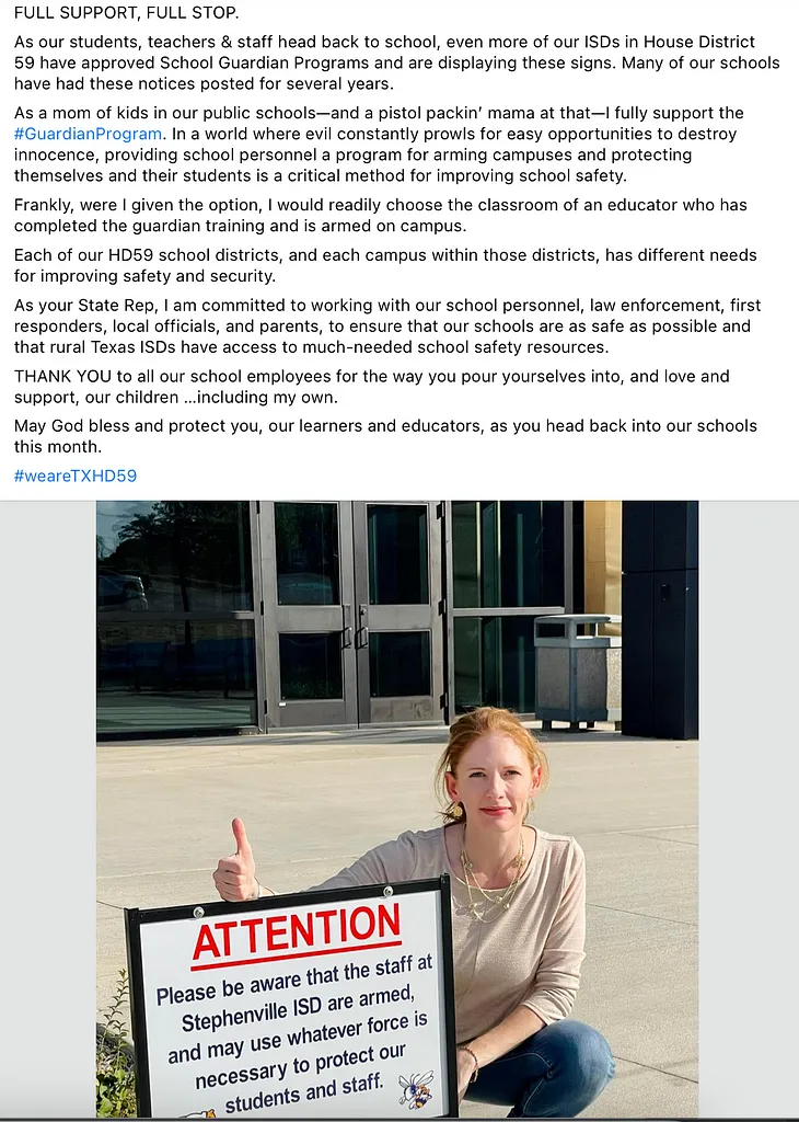 Image is a screenshot. The picture is of a red-headed white woman squatting next to a sign outside of a school. The sign reads, “ATTENTION-Please be aware that the staff at Stephenville ISD are armed, and may use whatever force is necessary to protect our students and staff. “ The text of the post is given at the end of this essay, as it won’t fit here.