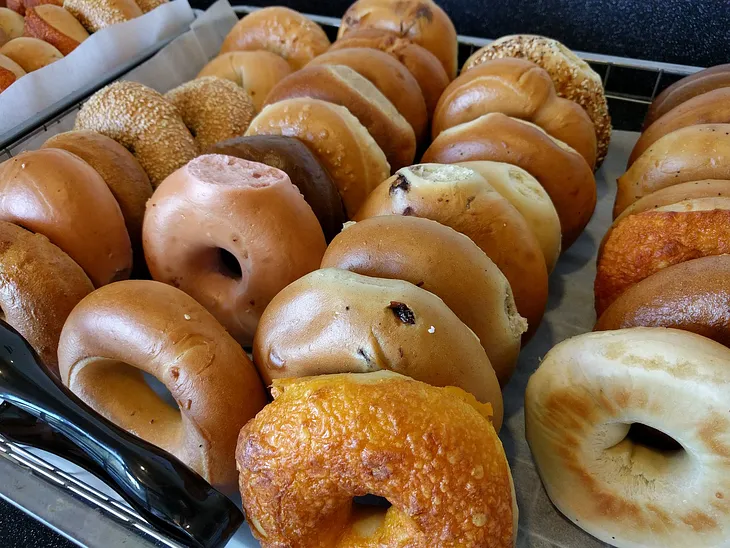 An assortment of bagel flavors upon a bakery tray.