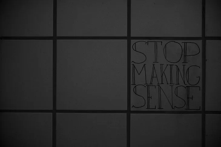 The words “Stop Making Sense” written in a Serif-based script on the wall of a bathroom stall.