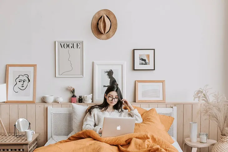 a woman looks at her laptop in bed, resting after realizing the value of going inward this season.