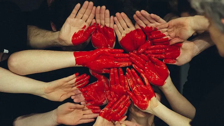 many human hands put together and painted red so they form pieces of a heart