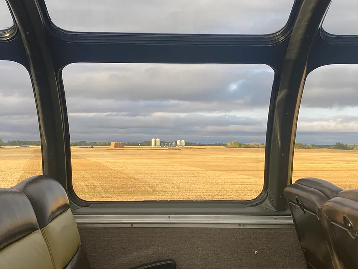 Grain elevators are on a bright golden field framed by the train window.