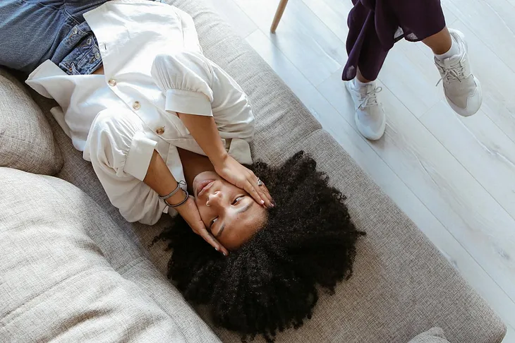 Photo of a distressed student lying on a couch next to someone listening to them, reminiscent of  a counseling session.