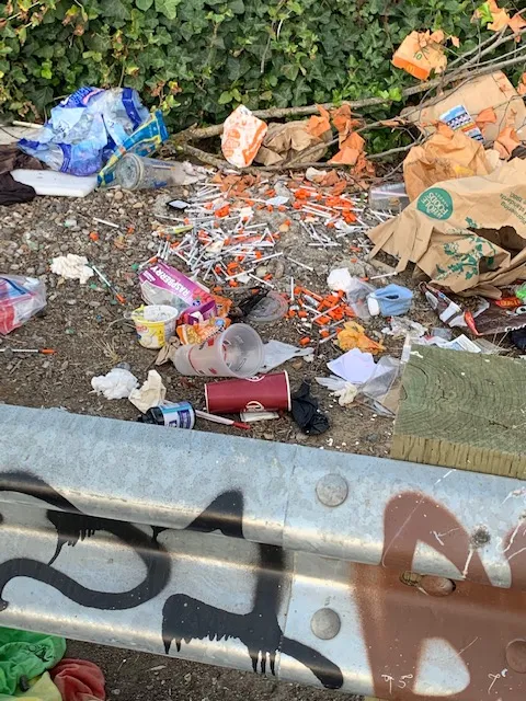 piles of used illicit drug use needles left on ground by homeless camp
