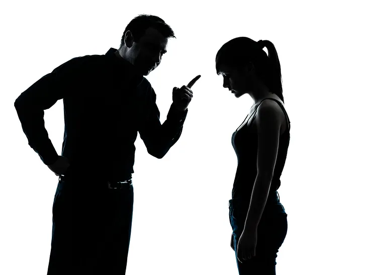 The silhouettes of a man pointing at a teenage girl.