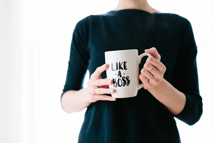 A photo of a woman in a black shirt holding a white coffee mug with “Like A Boss” on it.