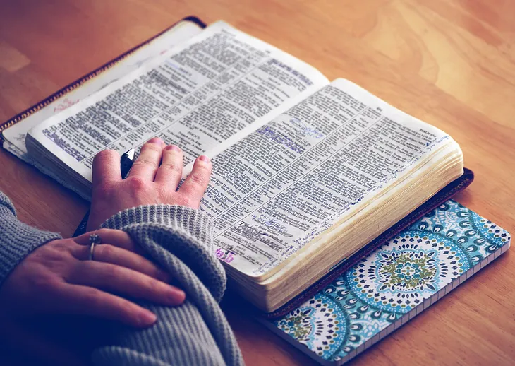 open bible on table with woman’s hands