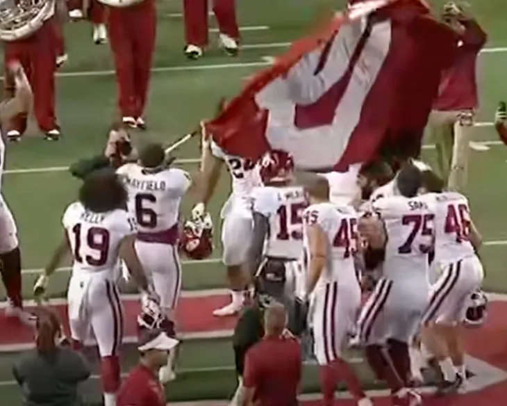 A group of University of Oklahoma football players, led by Baker Mayfield, plant an “OU” flag into the center of Ohio State’s 50-yard line.