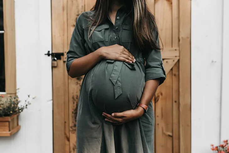 Pregnant woman wearing a green dress holding her stomach