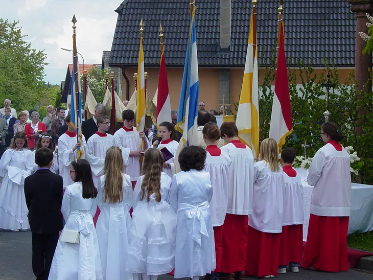 The town folk of Salmuenster (at least the Catholic majority) turn out in bridal white and funeral black to celebrate and acknowledge Blood Sunday near the city square festooned with colorful Church flags and banners.