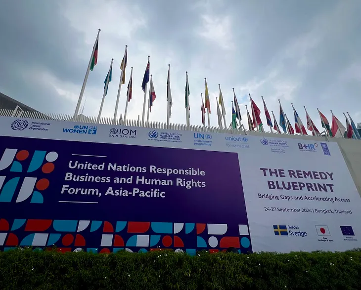 Sign reading United Nations Responsible Business and Human Rights Forum, Asia-Pacific in front of a row of flags in the entrance to the UN Building in Bangkok