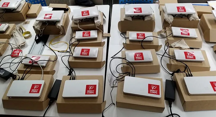 A set of WiFi routers and access points labeled with Mercy Corps stickers prepared for deployment