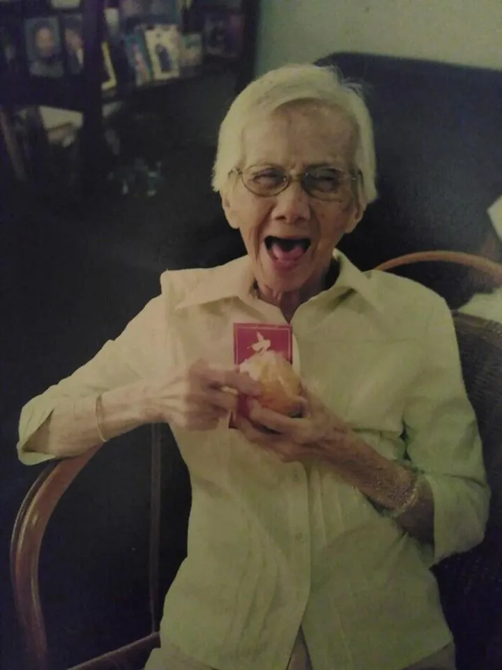 Picture of the Author’s maternal grandmother smiling as she holds a peeled mandarin orange and a red packet during Chinese New Year.