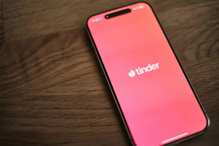 Smartphone on wooden table showing Tinder splash screen