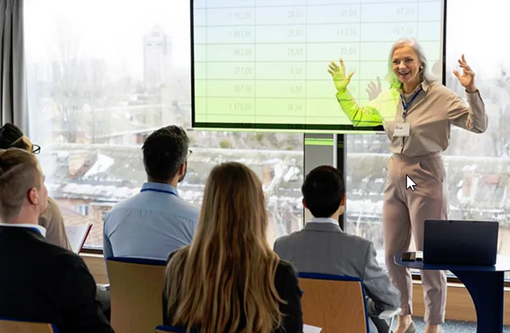 A photo of a woman giving a presentation to a group of people.