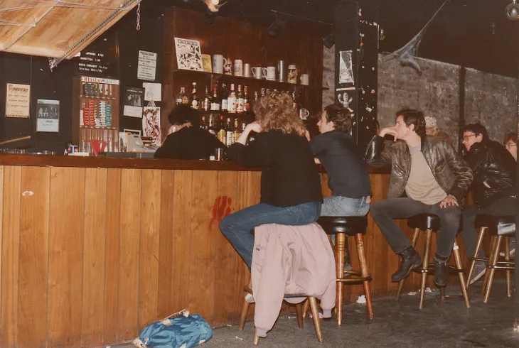 People seated on stools at a scruffy-looking bar.