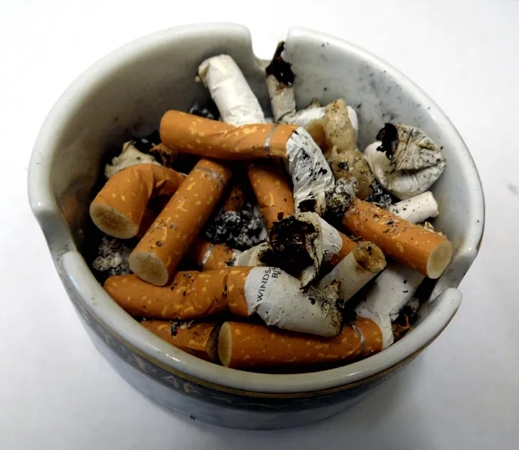 A circular ceramic ashtray that is filled with cigarette ends.