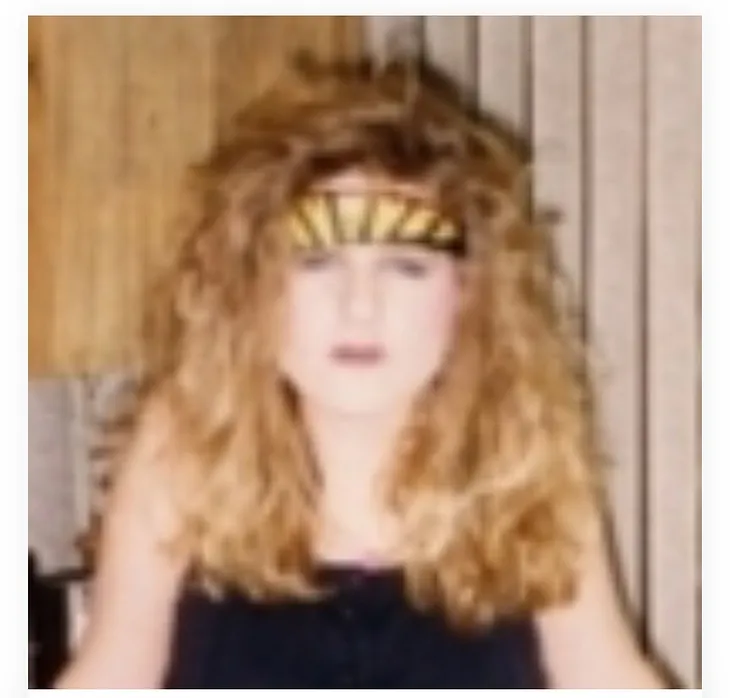 An old hazy photo of a teen girl with big hair and a sullen expression, wearing a Journey bandana.