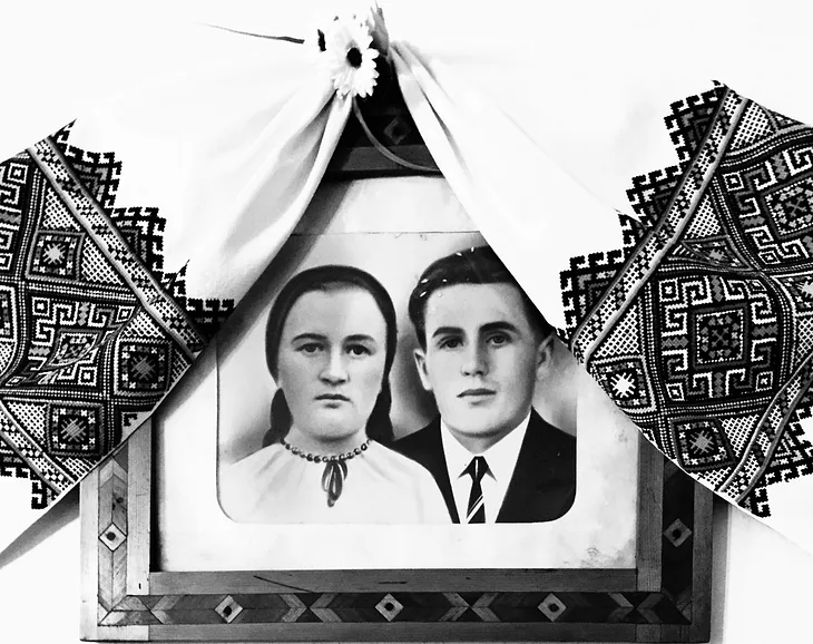 A black and white framed photograph of two people, draped by an embroidered hanging.