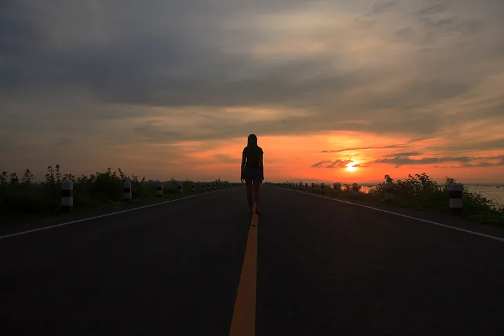 Girl walking alone at night on a deserted highway.