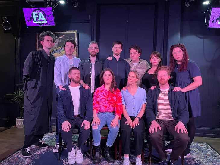 Performers standing and sitting on stage after an improv gig, posing with their hands on each other’s shoulders