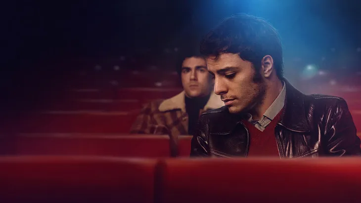 One man sits behind another in a hazy movie theatre.